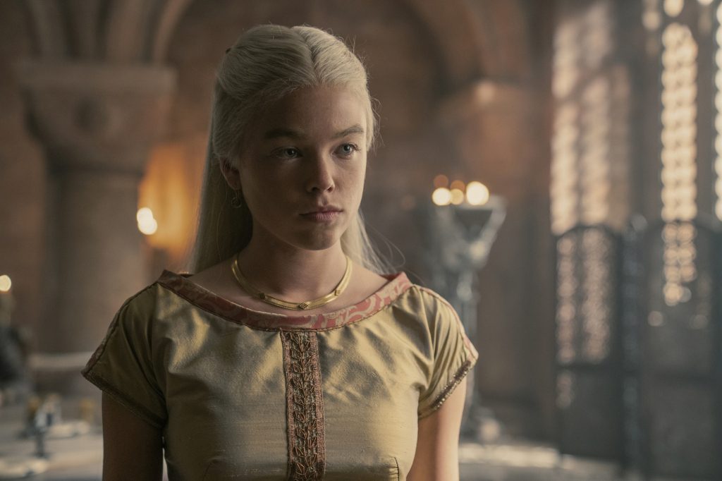 Millie Alcock trong vai Công chúa Rhaenyra Targaryen trong "Nhà rồng" Đang đứng trong một căn phòng, mặc một chiếc váy. 